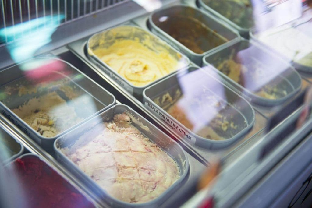 Freezer expositor mostrando potes de sorvete artesanal com consistência cremosa, demonstrando a baixa temperatura ideal para o endurecimento rápido e preservação da textura na confeitaria.