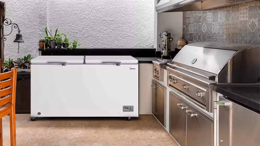 Freezer horizontal branco em área gourmet externa, com cozinha equipada com churrasqueira e armários de inox, perfeito para confeitaria.