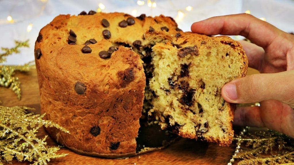 Foto em close de um Panetone Chocotone artesanal com gotas de chocolate, exibindo a maciez da massa e a sova correta. Uma fatia é destacada, mostrando a umidade e a uniformidade dos ingredientes.