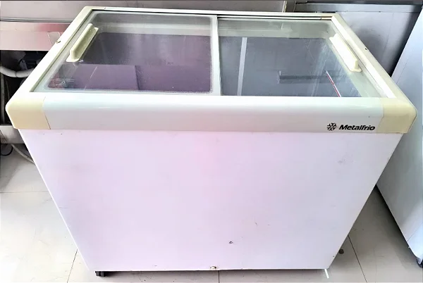Freezer horizontal expositor com tampa de vidro, ideal para a exibição de picolés e sorvetes organizados em caixas, otimizando a venda por impulso na confeitaria.