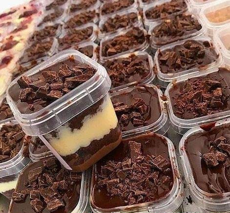 Grande produção em lote de bolo no pote de chocolate e creme, com cobertura de ganache e pedaços de chocolate em potes quadrados transparentes. Imagem ilustra a importância de otimizar o tempo para aumentar a escala de vendas.