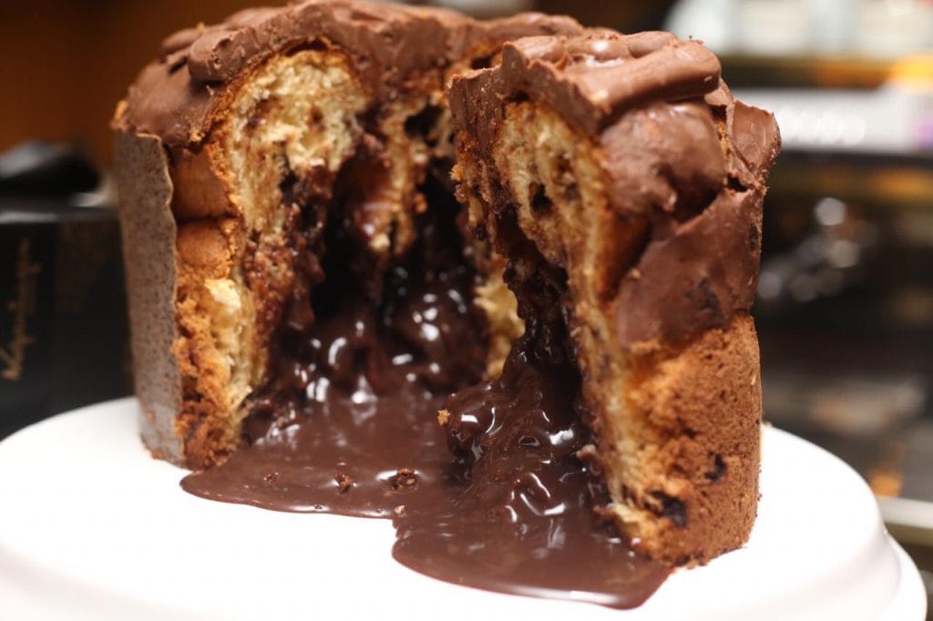 Panetone Língua de Gato cortado, exibindo recheio cremoso de chocolate escorrendo, coberto com chips de chocolate para garantir a crocância. Receita gourmet ideal para a venda de Natal.