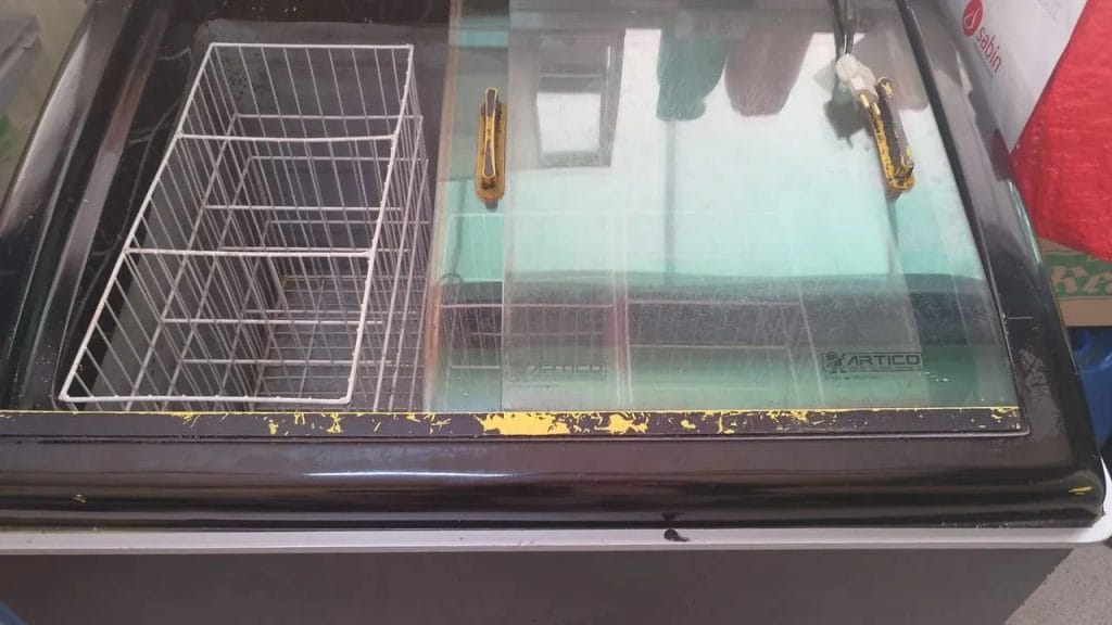 Visão superior de um freezer horizontal com tampa de vidro, exibindo cubetas de sorvete e açaí organizadas em fileiras, demonstrando o controle de estoque e análise de demanda.