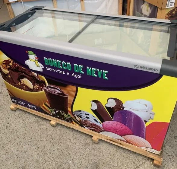 Freezer horizontal adesivado para sorvetes e açaí posicionado sobre um pallet de madeira em um galpão industrial, destacando o tamanho e a capacidade de armazenamento para pontos de venda.