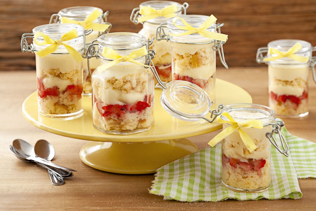 Bolo no pote de leite Ninho com morango em embalagens de vidro herméticas com laço de fita amarela, expostos em um suporte de bolo. Decoração e design que atraem o olhar do cliente para vender mais.