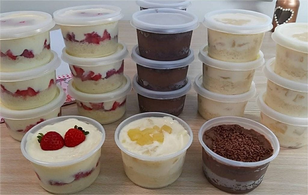 Diversos potes de Bolo no Pote com camadas de recheios cremosos (morango, chocolate, abacaxi) e coberturas, ilustrando a variedade e a estabilidade de texturas que não congelam.