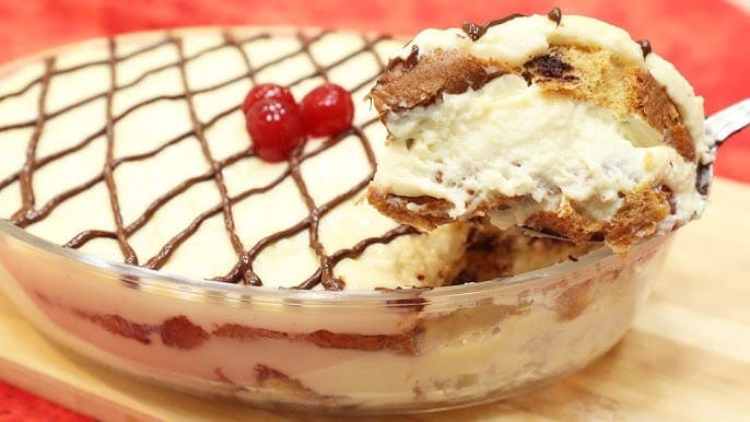 Porção de Panetone na Travessa (sobremesa de colher) sendo servida, destacando as camadas cremosas e a calda de chocolate. Uma Fotografia de Impacto que vende a experiência e o luxo da sobremesa de Natal.