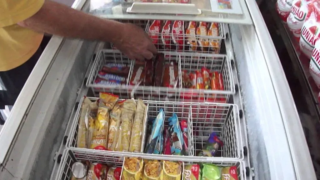 Visão interna de um freezer horizontal aberto, mostrando diversos sabores de picolés e potes de sorvete organizados em cestos metálicos, facilitando a aplicação do método FIFO e o controle de estoque.