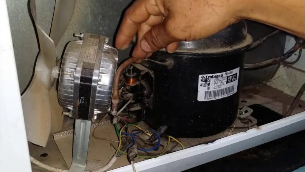 Técnico especializado em refrigeração realizando o conserto do compressor de um freezer, indicando falha técnica grave ou vazamento de gás refrigerante.