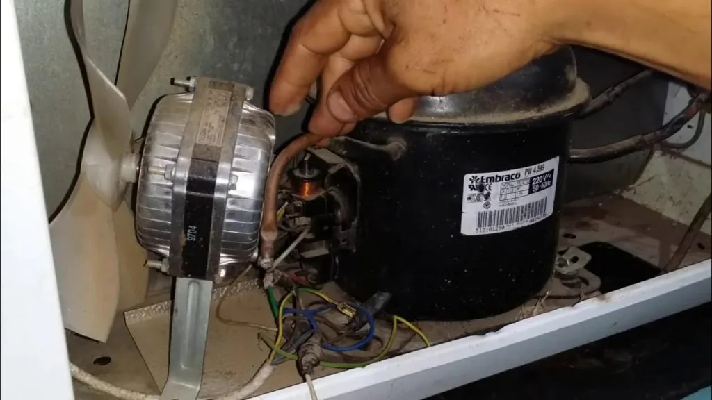 Técnico especializado em refrigeração realizando o conserto do compressor de um freezer, indicando falha técnica grave ou vazamento de gás refrigerante.