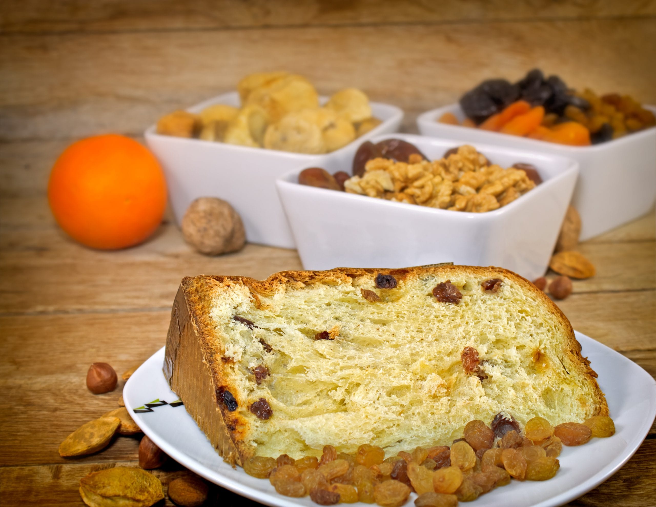 Fatia de panetone vegano (ou sem ingredientes de origem animal) com frutas cristalizadas e passas, cercada por ingredientes de alta qualidade. Ideal para atender o nicho de mercado com receitas gourmet e zero açúcar.