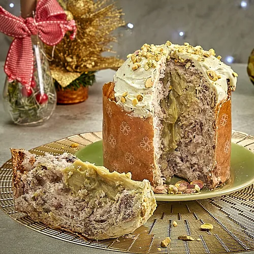 Panetone de Pistache Gourmet recheado e cortado, com cobertura de pistache picado, em Cenário de Natal Clean. A imagem demonstra o Foco no Panetone, ideal para transmitir exclusividade e qualidade através da Fotografia.