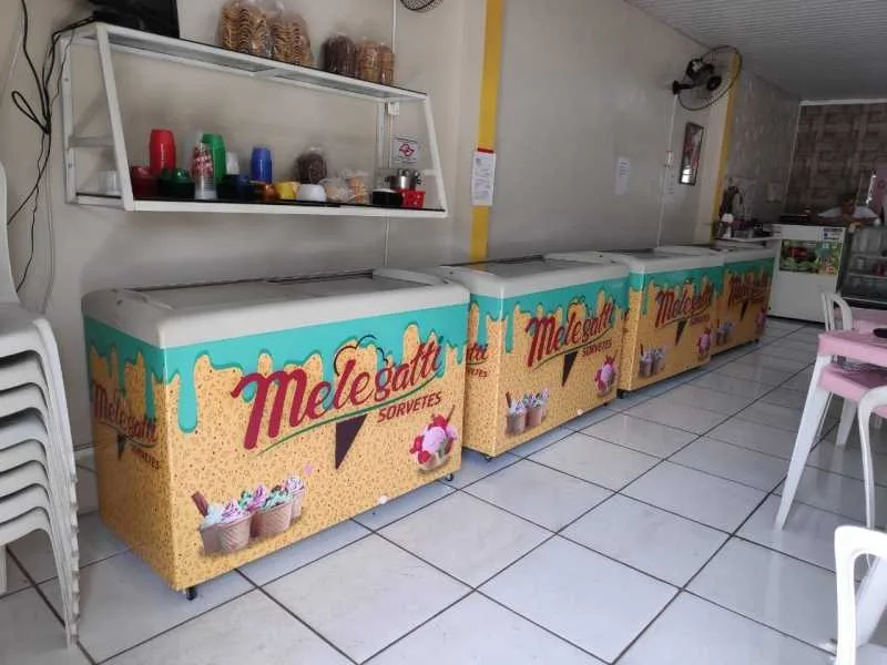 Fileira de freezers horizontais expositores com adesivagem personalizada da marca Melegatti Sorvetes, organizados em uma sorveteria, demonstrando um investimento seguro em equipamentos de qualidade.