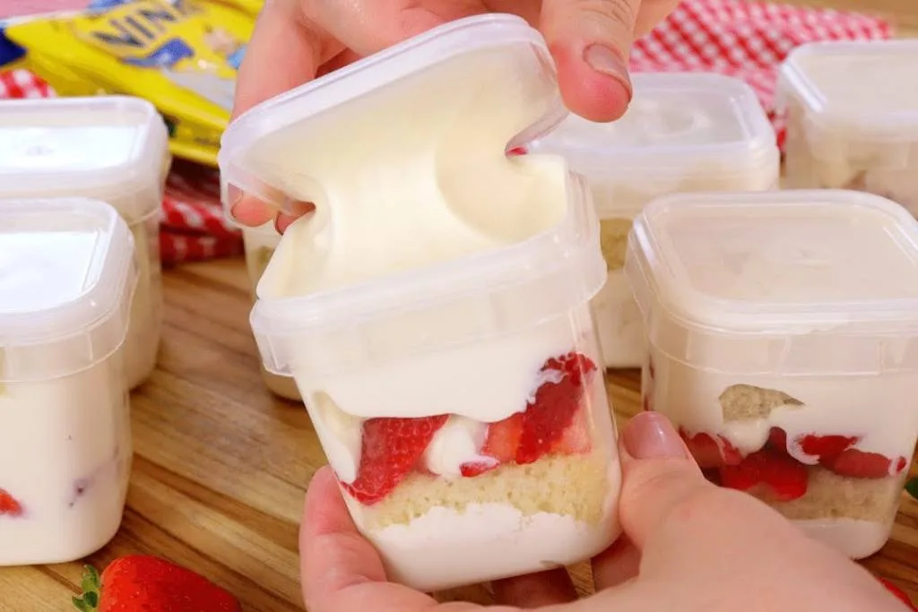 Montagem do bolo no pote de Leite Ninho com Morango (um dos sabores mais vendidos), destacando a cremosidade do recheio gourmet. A imagem ilustra as tendências de confeitaria para 2025 e o potencial de lucro.