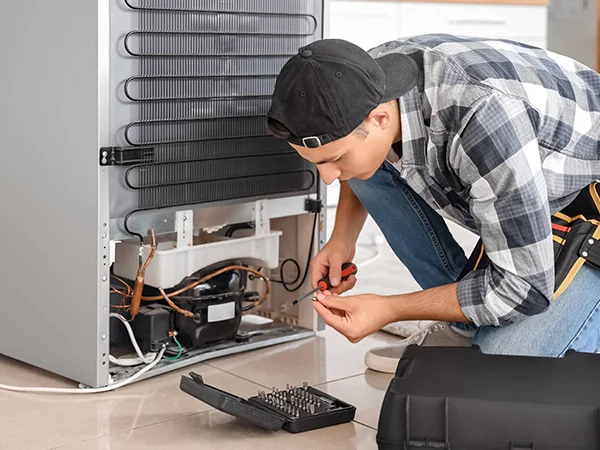 Técnico de refrigeração inspecionando o condensador e o compressor de um freezer horizontal, verificando problemas de superaquecimento e falta de resfriamento.