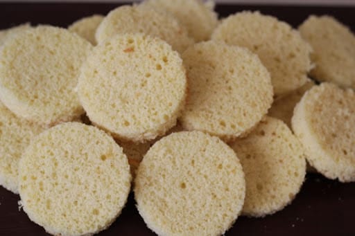 Rodelas cortadas de massa de pão de ló, empilhadas. Esta massa leve é ideal para o Congelamento, pois retém a umidade e a maciez após o descongelamento, otimizando a Escala de Produção de Bolo no Pote.