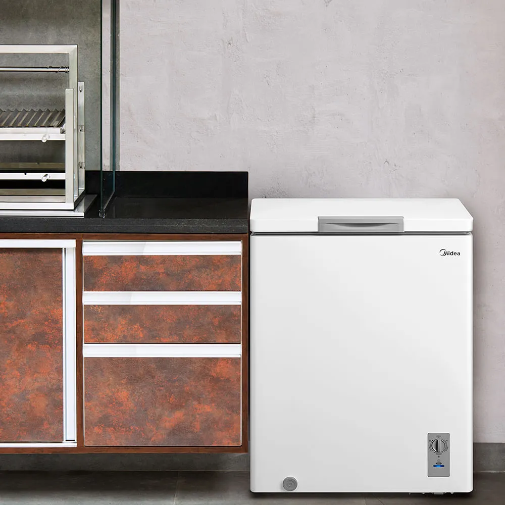 Freezer horizontal Midea de 145 litros na cor branca, posicionado em uma cozinha moderna com marcenaria em tons de madeira e iluminação pendente, destacando seu design compacto e funcional.