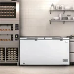Freezer horizontal Midea de duas portas na cor branca instalado em uma cozinha profissional ao lado de fornos de panificação, destacando sua robustez e capacidade para pequenos negócios.