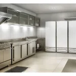 Cozinha profissional de confeitaria com três freezers verticais brancos alinhados ao lado de bancada de inox e fogão industrial.
