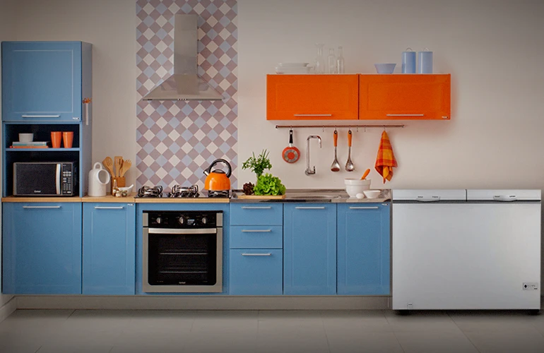 Cozinha planejada moderna com armários azuis e laranjas, destacando um freezer horizontal branco de duas tampas posicionado ao lado da bancada, exemplificando a retenção de ar frio.
