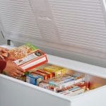 Pessoa organizando alimentos congelados dentro de um freezer horizontal branco de uma das melhores marcas do mercado, destacando o amplo espaço interno e a conservação térmica.