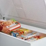 Pessoa organizando alimentos congelados dentro de um freezer horizontal branco de uma das melhores marcas do mercado, destacando o amplo espaço interno e a conservação térmica.
