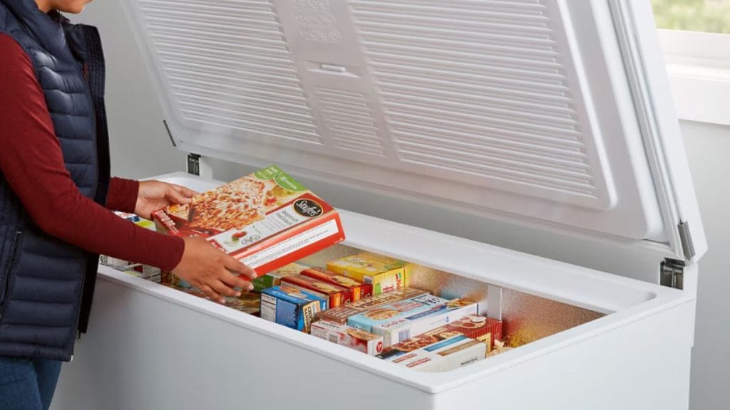 Pessoa organizando caixas de alimentos congelados dentro de um freezer horizontal aberto e iluminado, representando o teste prático de capacidade e organização.
