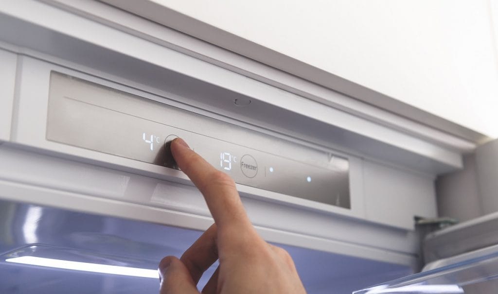 Mão ajustando a temperatura em um painel digital de freezer, exibindo 4°C e -19°C, ilustrando o controle de intensidade entre os modos de refrigeração e congelamento.