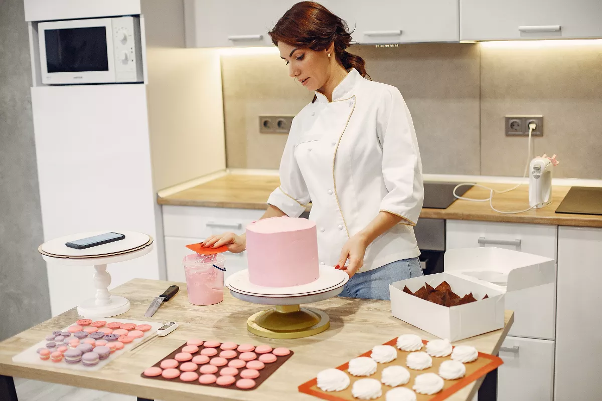 Confeiteira profissional preparando um bolo em cozinha equipada, representando oportunidades de parceria e divulgação para negócios de confeitaria