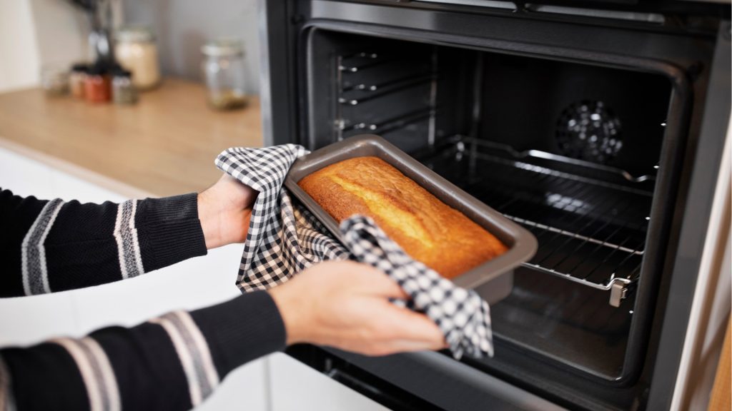 Pessoa retirando um bolo assado de um forno elétrico em uma cozinha de confeitaria