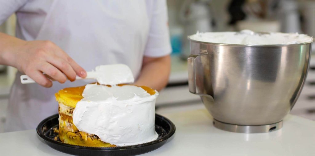 Profissional preparando a cobertura de um bolo durante uma atividade prática de confeitaria